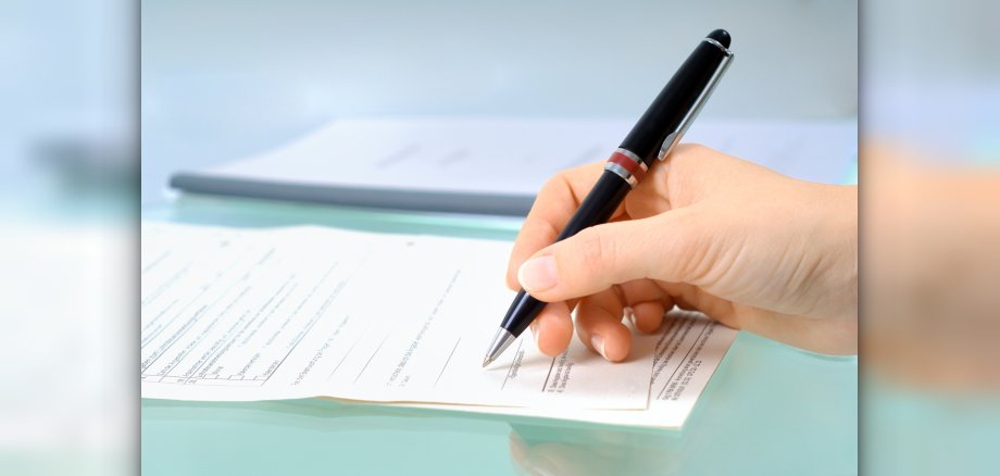 Hand with black pen signs a form.