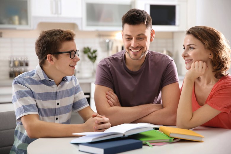 Teenagers doing homework with their parents Boy sits at the table with his parents. There are school books on the table.