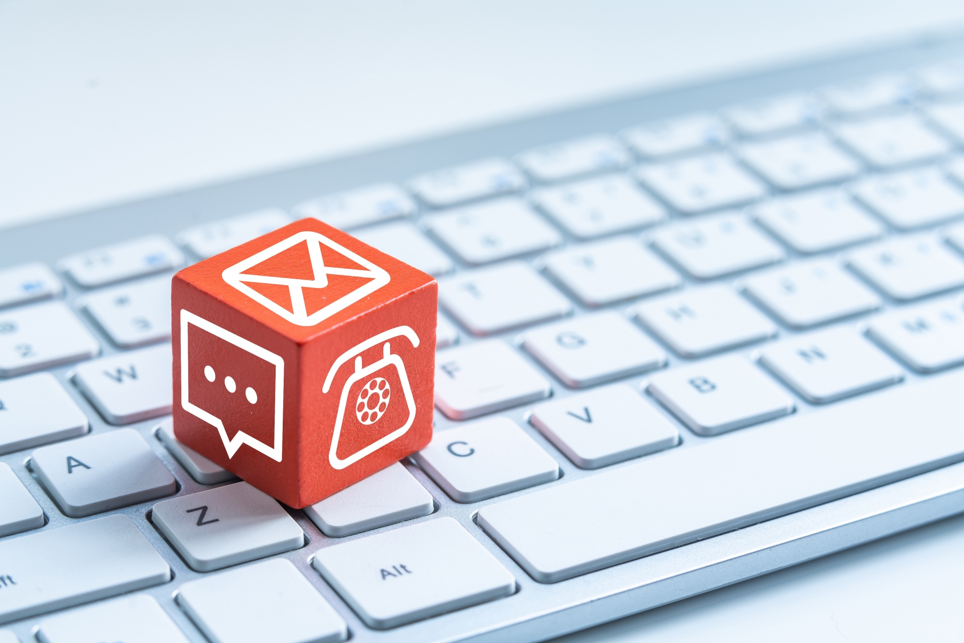 Red cube with various contact symbols (telephone, chat, envelope) lies on a white computer keyboard.