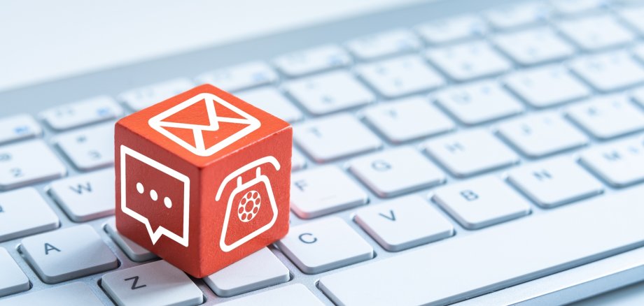 Red cube with various contact symbols (telephone, chat, envelope) lies on a white computer keyboard.
