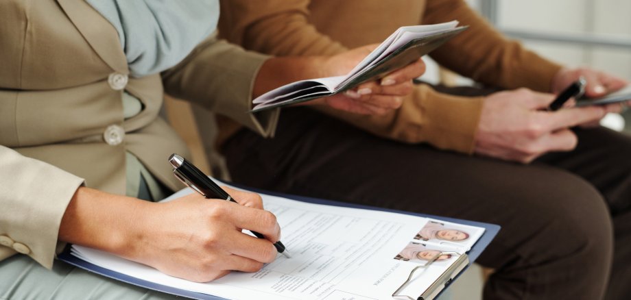 An unrecognisable woman sits on a chair in a government office and fills out an application form while waiting for her appointment.