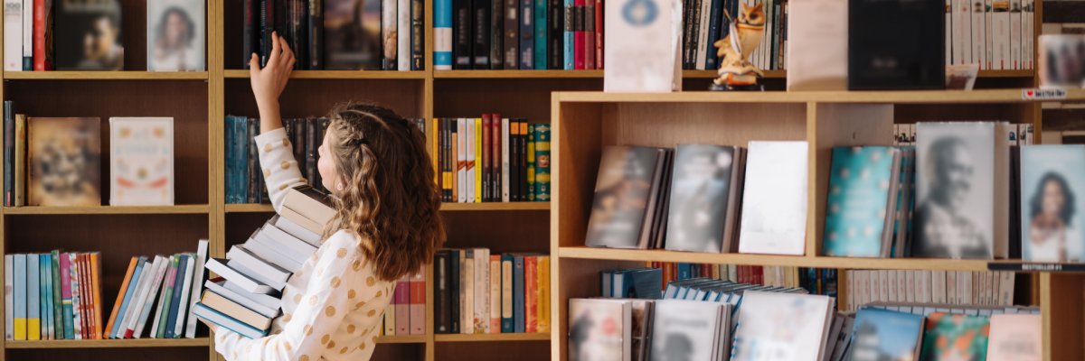 Une belle jeune fille tient une pile de livres alors qu'elle est debout parmi les livres dans la librairie.